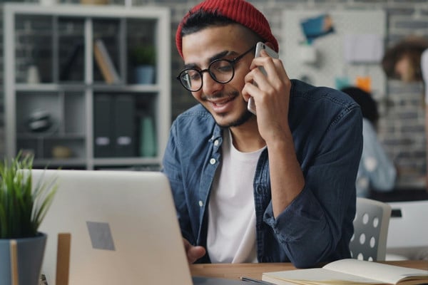 man talking on the phone as he looks at a laptop.